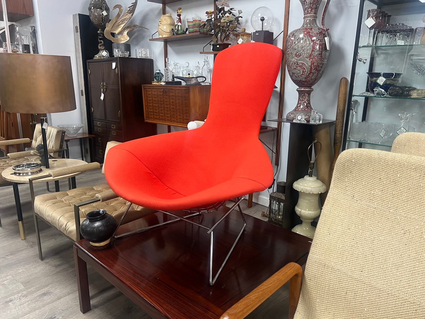 A bright red Bertoia Bird chair on a chrome rod base, beside a dark wood coffee table.