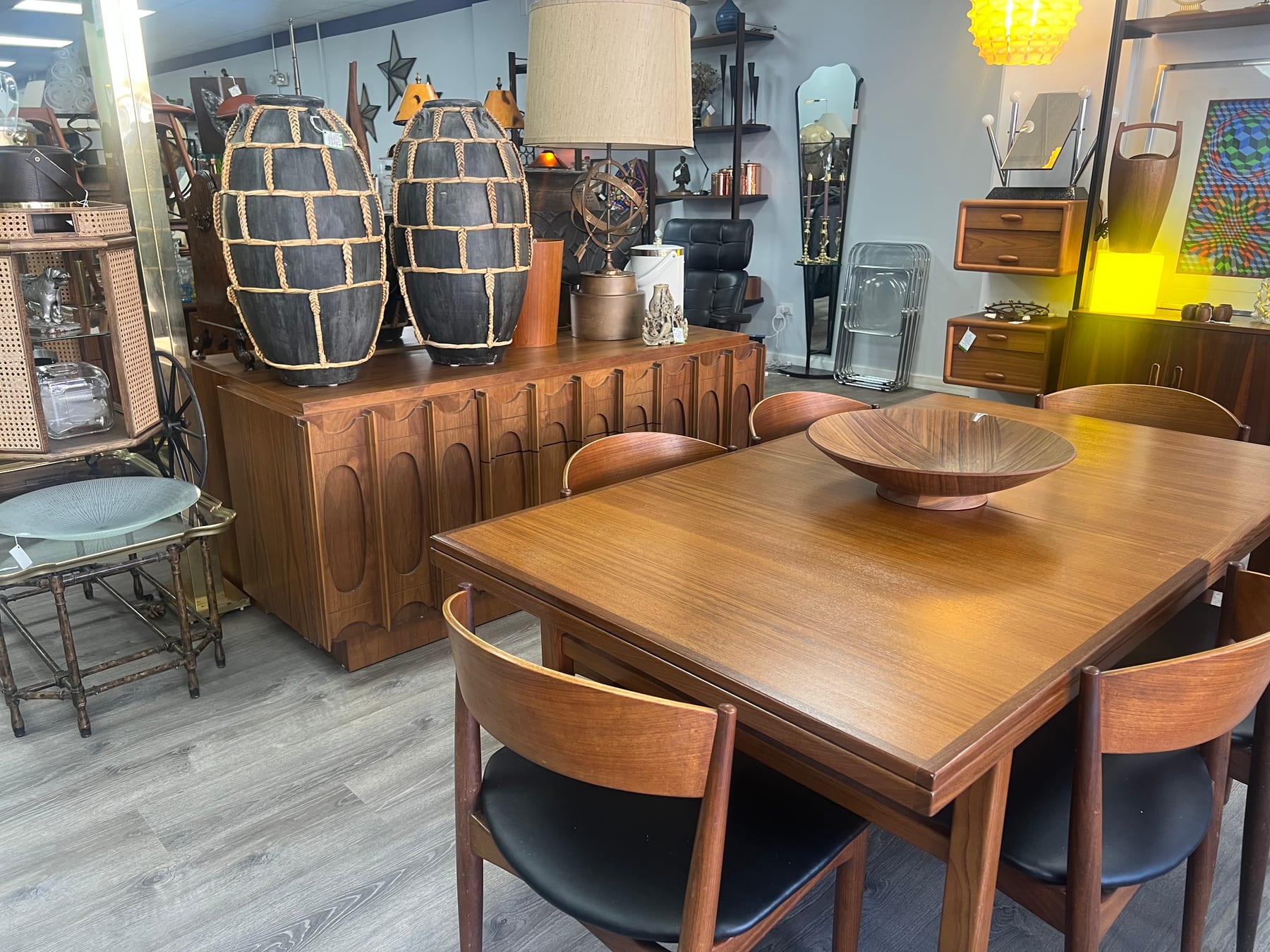 A walnut dining table with a Brutalist-front credenza, woven pendant lamps, and a teak fruit bowl.