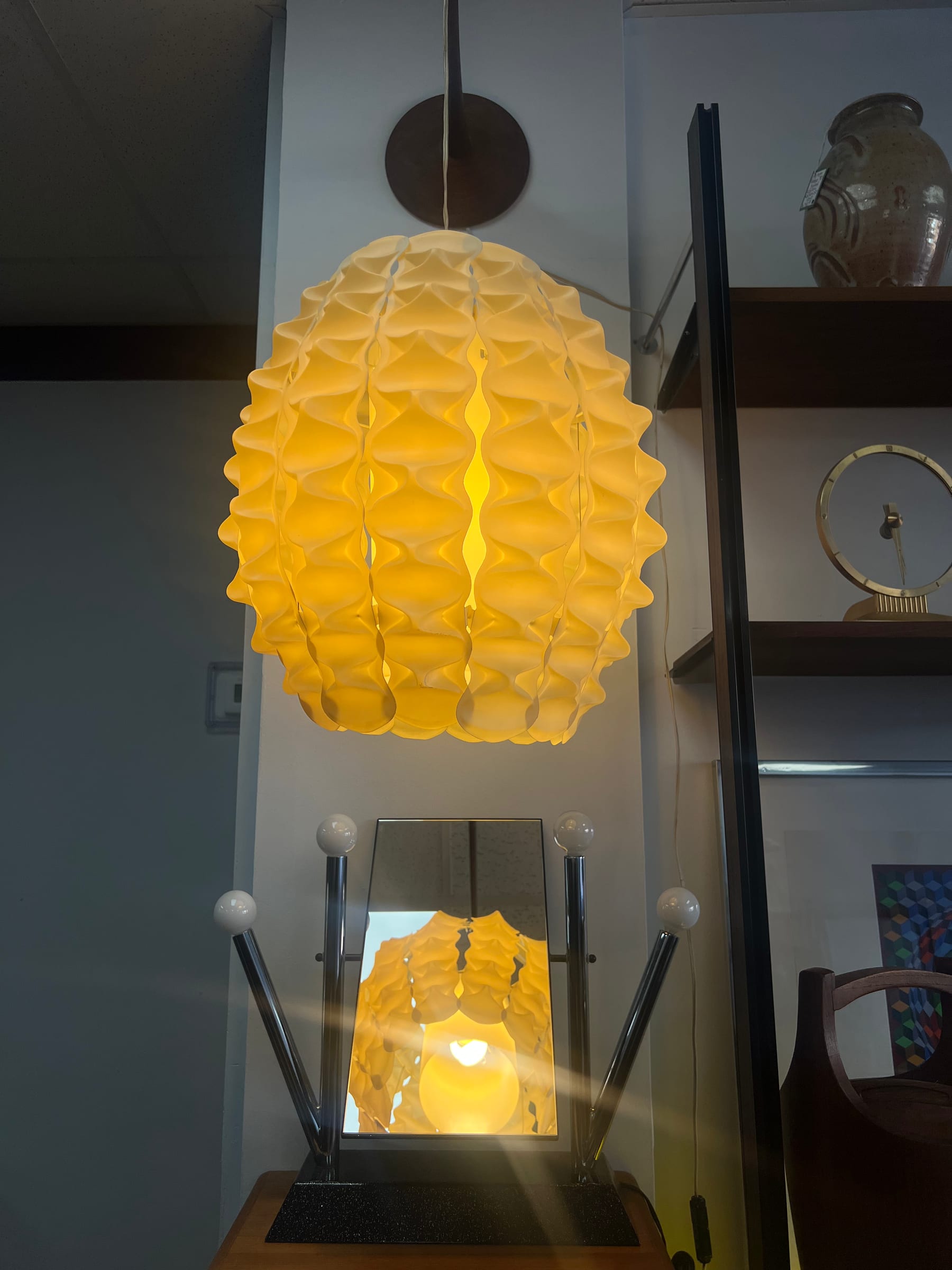 A tall amber-glass pendant lamp suspended over an inlaid mirror and a set of MCM shelves.